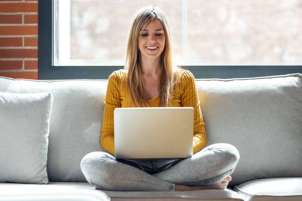 Laukaus kaunis nuori nainen työskentelee hänen laptop istuessaan sohvalla kotona. - Valokuva, kuva