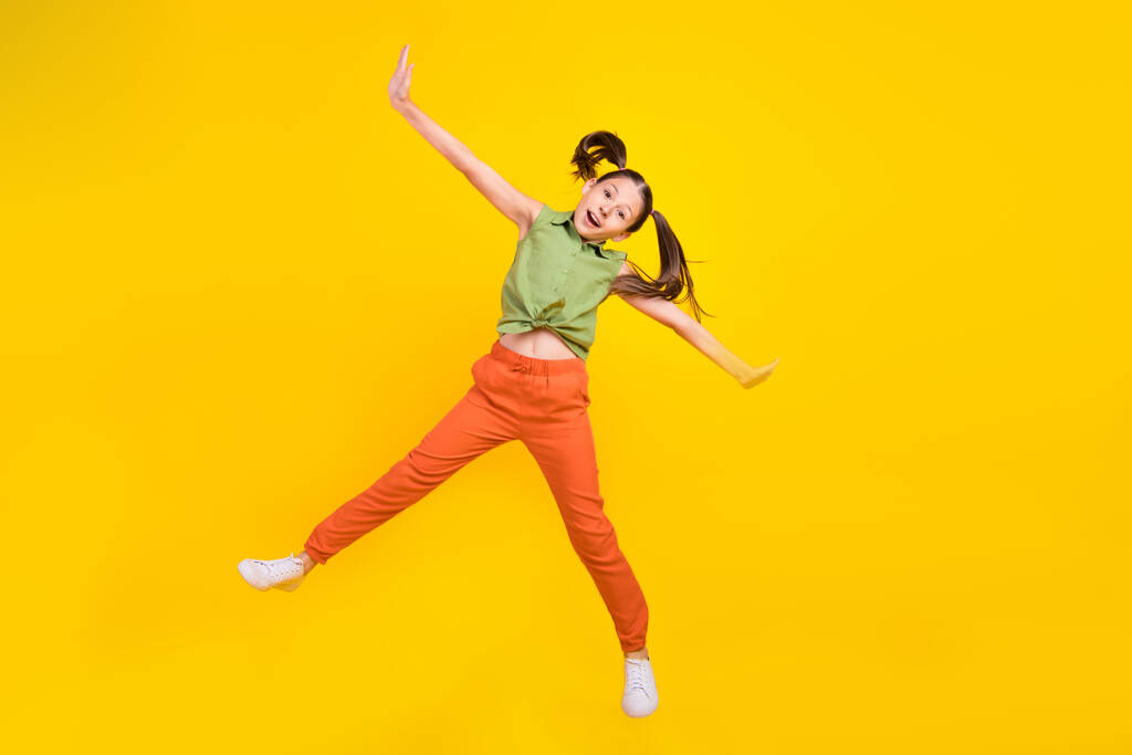 Foto van mooie zoete student meisje dragen groene shirt glimlachen springen hoge handen armen zijden geïsoleerde gele kleur achtergrond - Foto, afbeelding