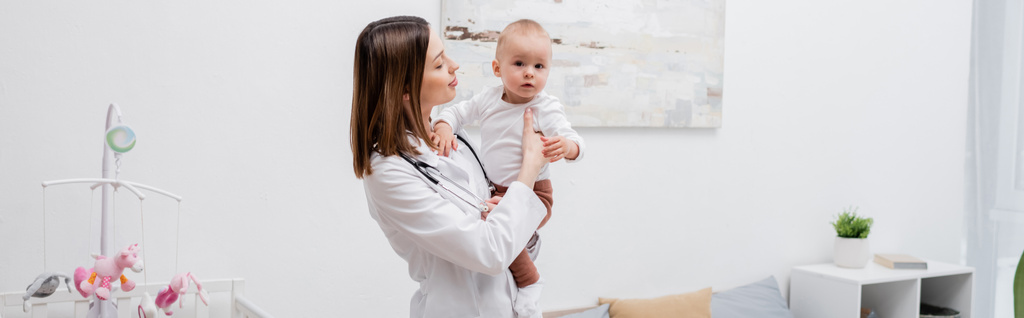 Jeune médecin de famille en berceau blanc tenant bébé garçon à la maison, bannière  - Photo, image