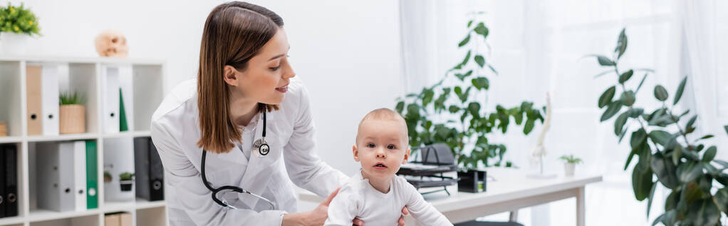Brunette pédiatre regardant bébé garçon à la clinique, bannière  - Photo, image