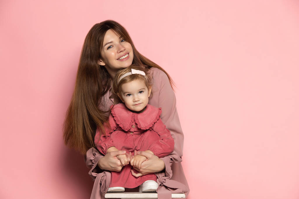 Αγκαλιές. Ενθουσιασμένη νεαρή γυναίκα και νήπιο, στοργική μητέρα και κόρη απομονωμένες σε ροζ φόντο στούντιο. Γιορτή της Μητέρας. Έννοια της οικογένειας, παιδική ηλικία, μητρότητα - Φωτογραφία, εικόνα
