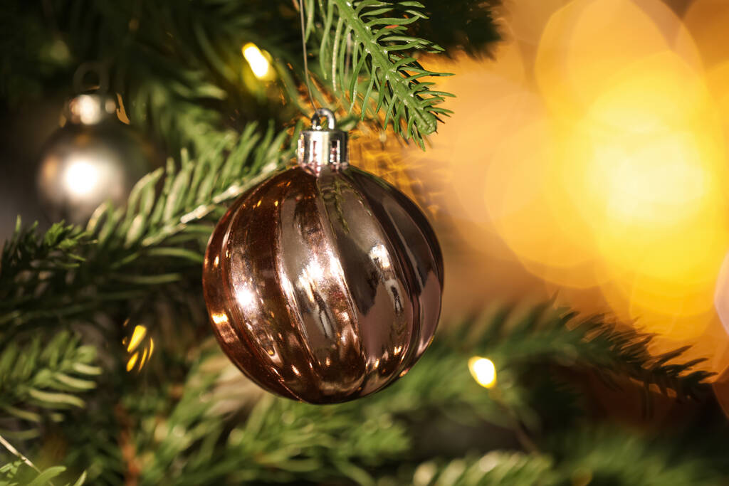 Piękna świecąca świąteczna bombka wisząca na choince przed rozmytymi światłami bajki, zbliżenie. Miejsce na tekst - Zdjęcie, obraz