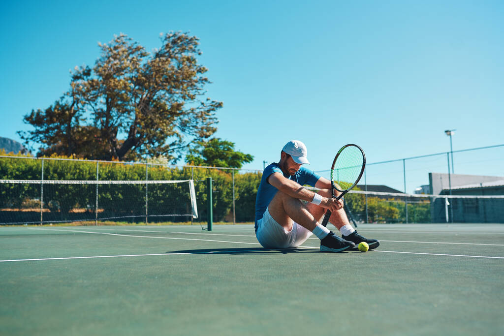 Niemand is een mislukkeling totdat ze stoppen met proberen. Full length shot van een jonge mannelijke tennisser zich moe voelen en zitten op een tennisbaan buiten. - Foto, afbeelding