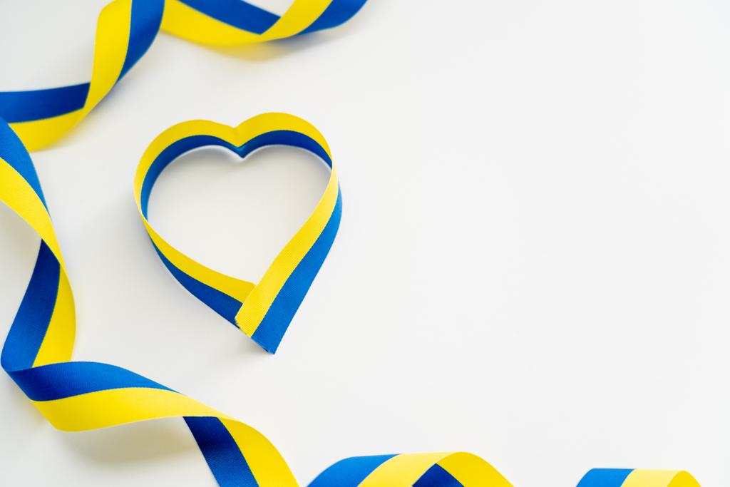 Bovenaanzicht van blauwe en gele linten in hartvorm op witte achtergrond - Foto, afbeelding
