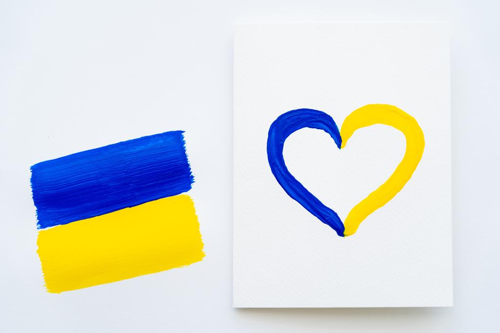 Vista superior de la tarjeta con signo de corazón pintado y bandera ucraniana sobre fondo blanco  - Foto, imagen