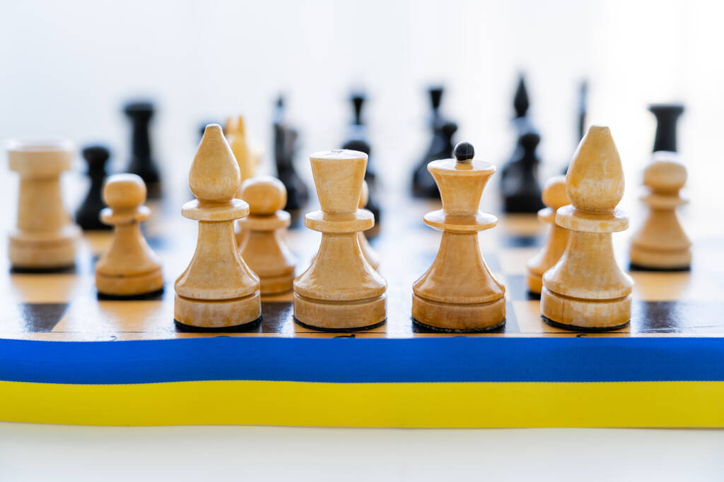 Vista de cerca de la cinta azul y amarilla cerca del ajedrez en el tablero de ajedrez sobre fondo blanco  - Foto, Imagen