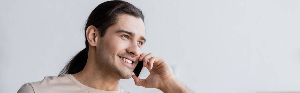 счастливый мужчина с длинными волосами, говорящий на смартфоне, баннер - Фото, изображение