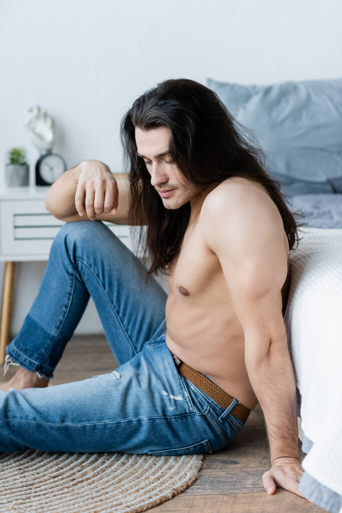 attente shirtloze man met lang haar in de buurt van bed - Foto, afbeelding