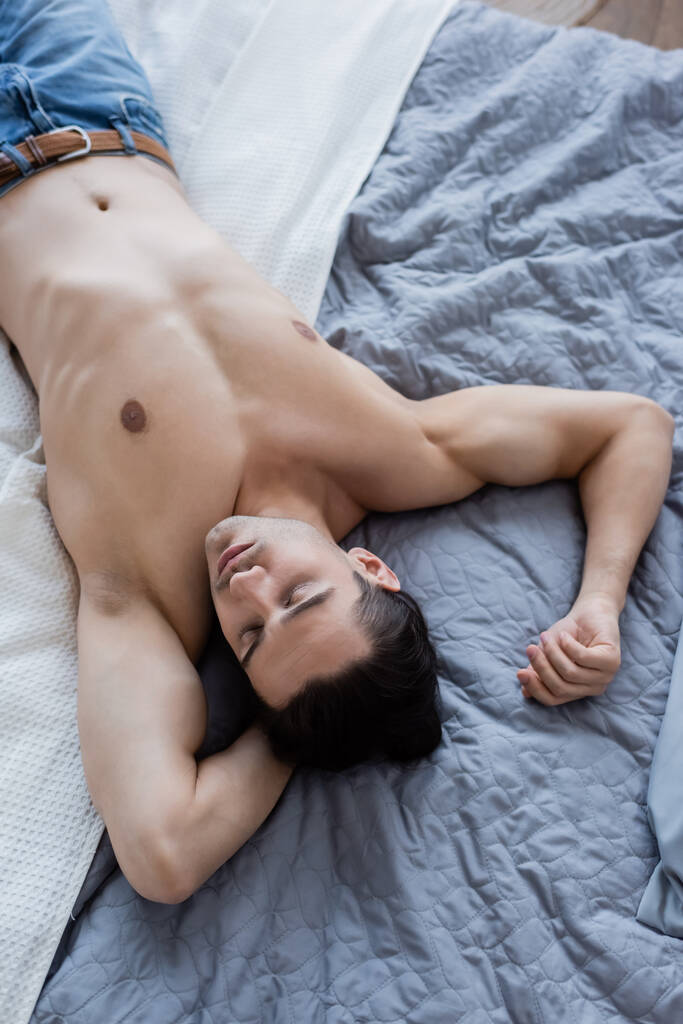 top view of shirtless man in jeans lying on bed - Photo, Image
