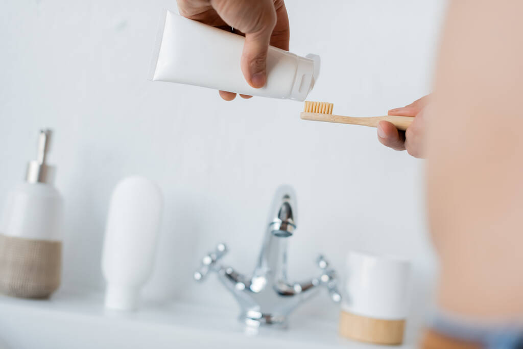 Ausgeschnittene Ansicht eines Mannes, der im Badezimmer Zahnpasta auf die Zahnbürste drückt - Foto, Bild
