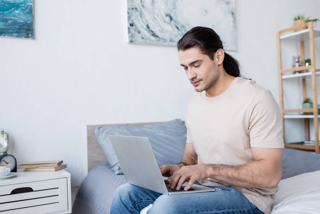 freelancer with long hair sitting on bed and using laptop  - Photo, Image