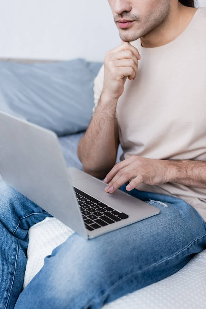 przycięty widok freelancer siedzi na łóżku i za pomocą laptopa  - Zdjęcie, obraz