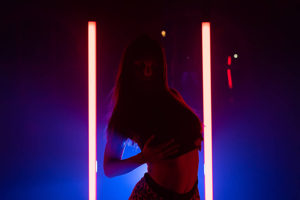 Seksowna kobieta tańcząca na świecącym tle lamp LED. Wygląda uwodzicielsko. Niebieskie studio dymne. - Zdjęcie, obraz