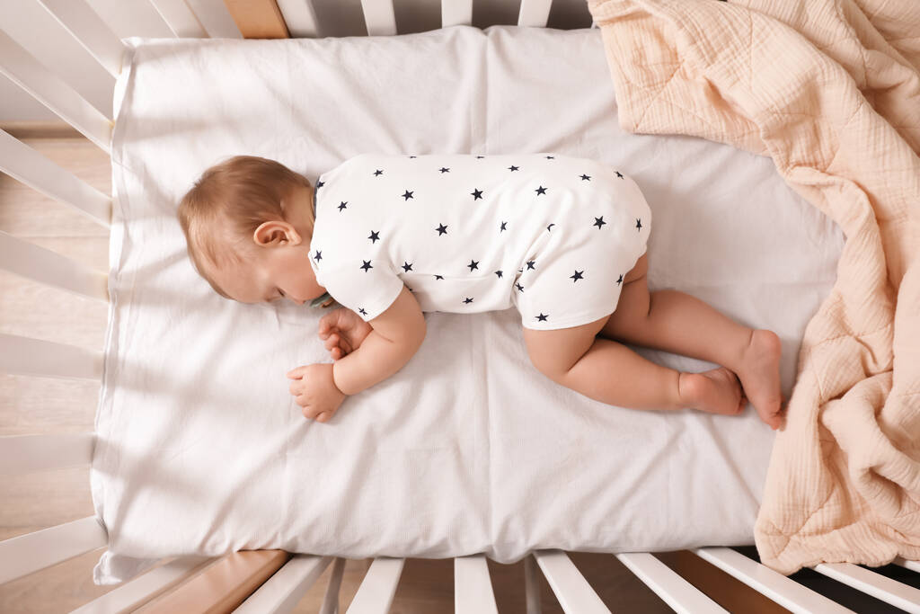 Imádnivaló kis baba cumival alszik bölcsőben beltérben, felülnézet - Fotó, kép