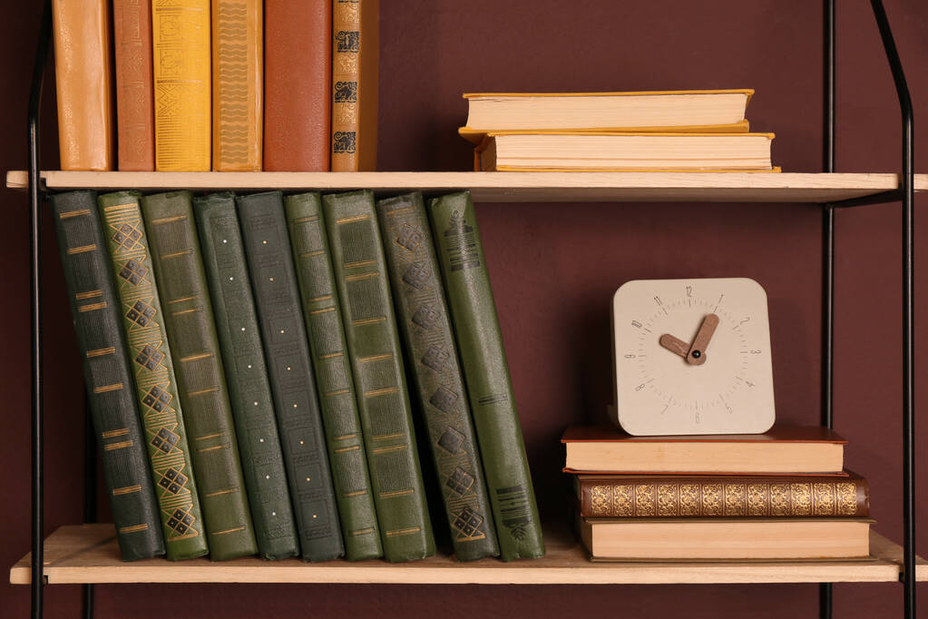 Estantes con diferentes libros y reloj en la pared marrón - Foto, imagen