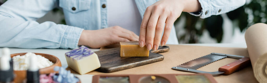 Oříznutý pohled na řemeslnici vyrábějící mýdlo na řezacím prkně v blízkosti zásob, banner  - Fotografie, Obrázek
