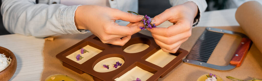 Vue recadrée de l'artisan tenant des fleurs près de savon fait à la main dans un moule en silicone à la maison, bannière  - Photo, image