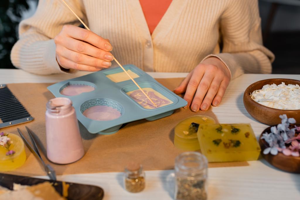 Vista cortada de artesã fazendo padrão no sabão no molde de silicone perto de suprimentos na mesa  - Foto, Imagem