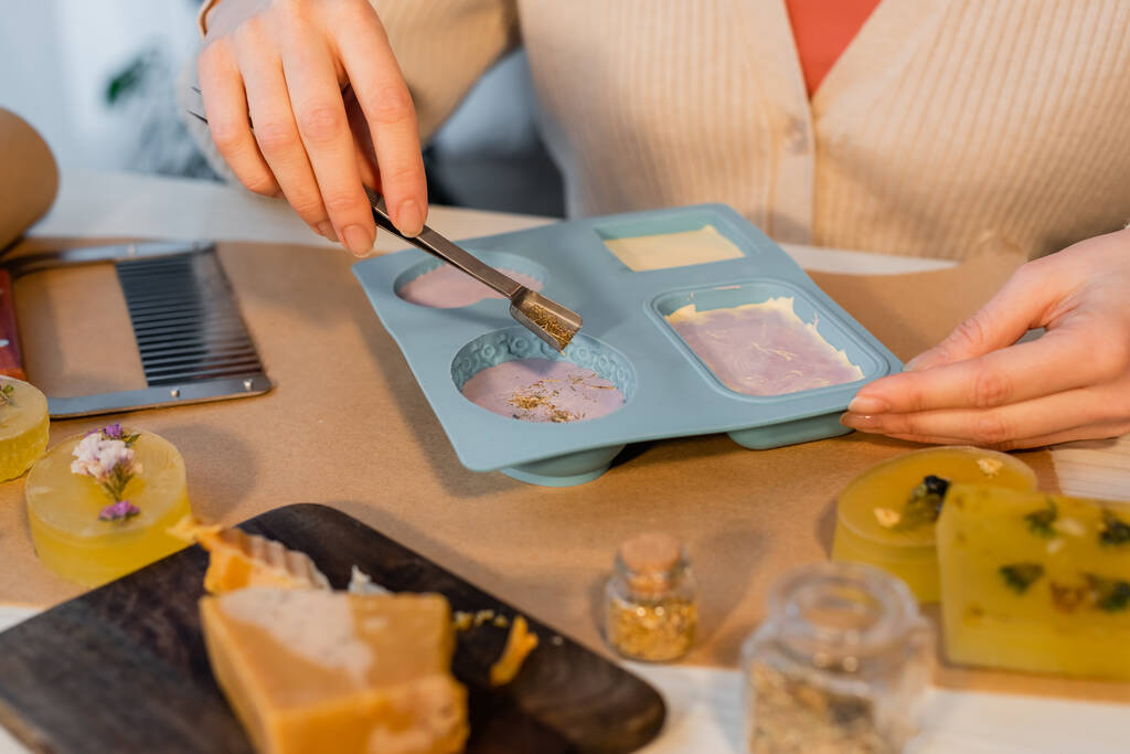 テーブルの上のクラフト紙の上にシリコーン型に石鹸にサフランを注ぐ職人の女性の作物ビュー - 写真・画像