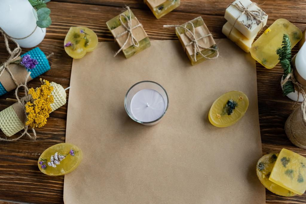 Bovenaanzicht van handgemaakte kaarsen en zeeprepen op ambachtelijk papier op houten ondergrond  - Foto, afbeelding