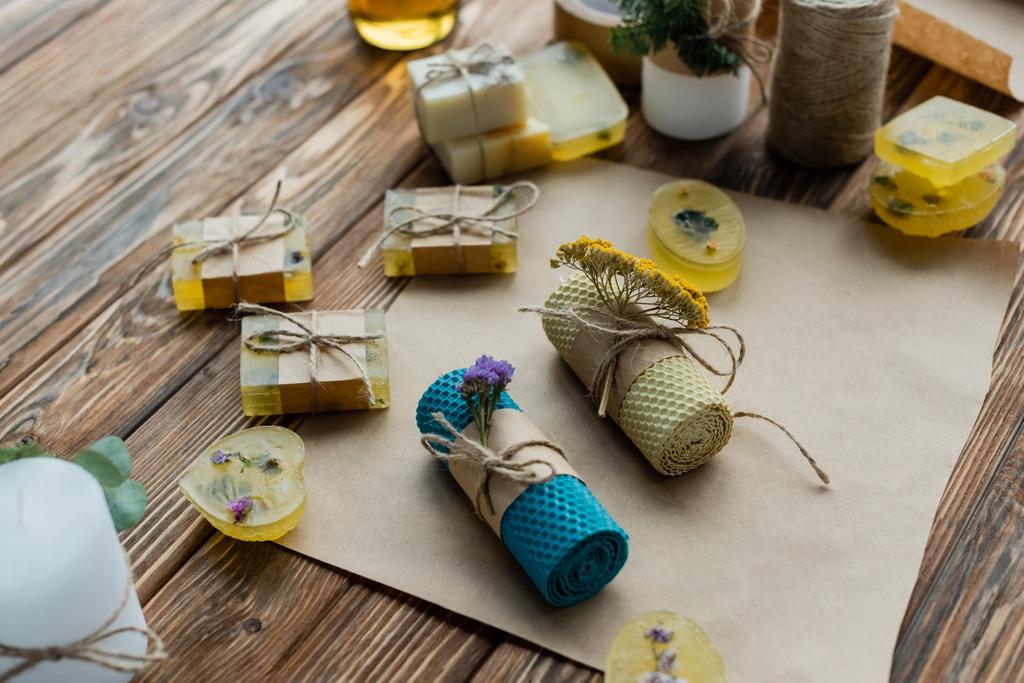 High angle view of handmade candles with flowers on craft paper near soap on wooden surface - Photo, Image