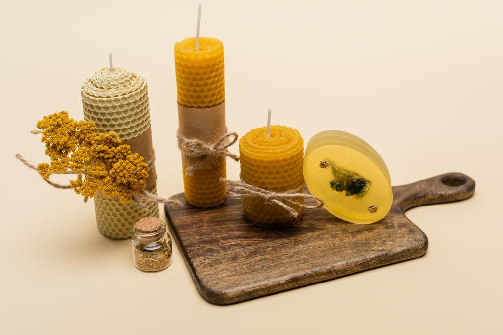 Velas hechas a mano y jabón con flores en tabla de cortar sobre fondo beige  - Foto, imagen