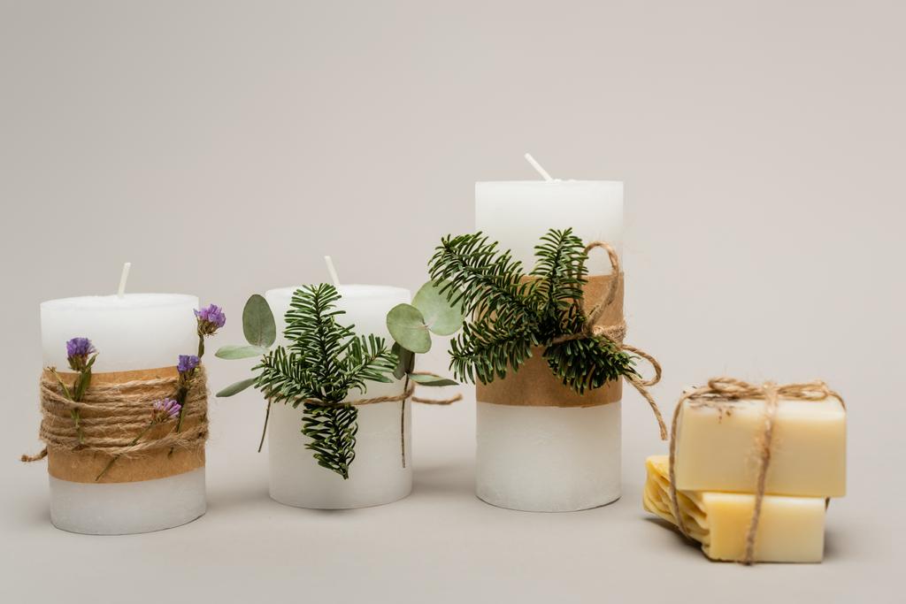 Velas hechas a mano con plantas cerca de barras de jabón borrosas sobre fondo beige  - Foto, imagen