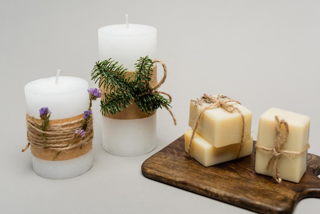 Kynttilät kasveilla ja saippuatangoilla leikkuulaudalla harmaalla pohjalla  - Valokuva, kuva