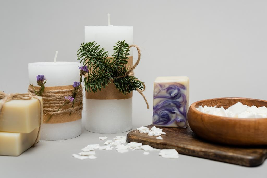 Ремесленное мыло возле свечей с растениями на разделочной доске на сером фоне  - Фото, изображение