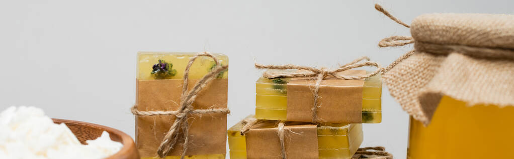 Detailní pohled na ručně vyráběné mýdlové tyčinky a vločky v blízkosti medu izolované na šedé, banner  - Fotografie, Obrázek