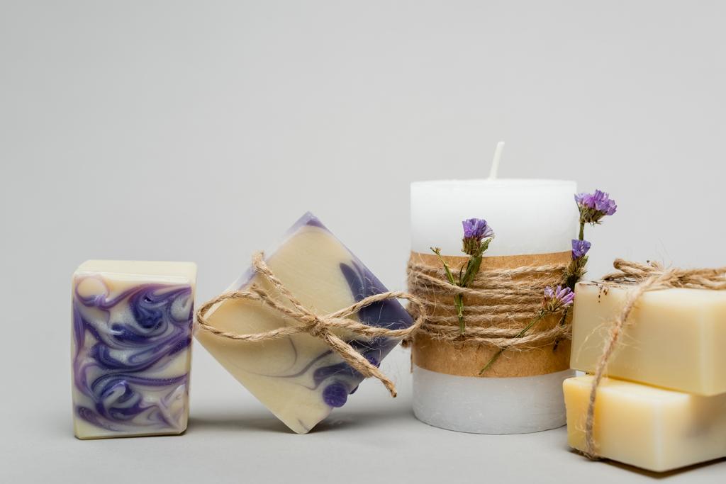 Jabón hecho a mano cerca de la vela con flores sobre fondo gris  - Foto, Imagen