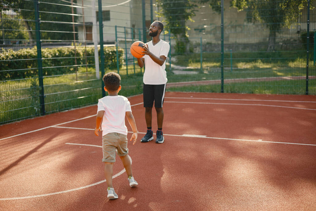 Μαύρος με γιο που παίζουν μπάσκετ στο γήπεδο μαζί. - Φωτογραφία, εικόνα