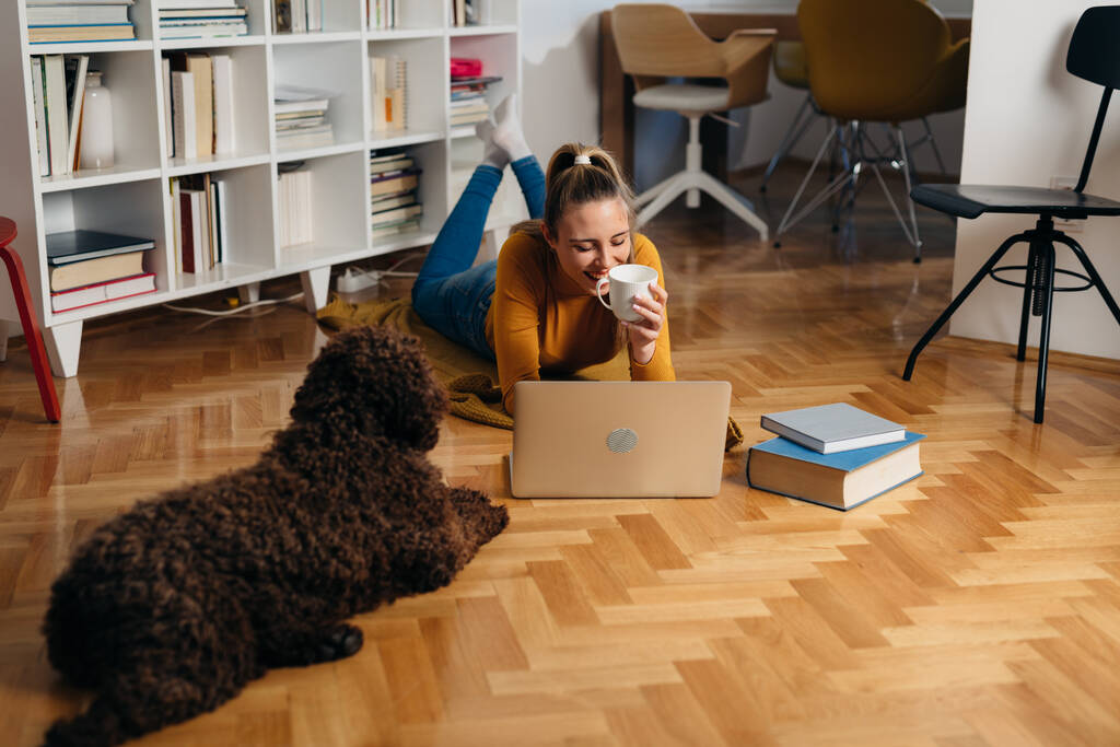 woman working on laptop computer with companionship of her dog at home - Photo, Image