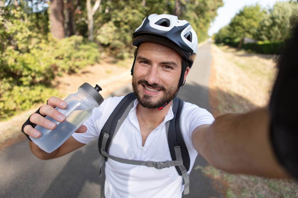 ciclista masculino sosteniendo botella de agua y tomando selfie - Foto, imagen