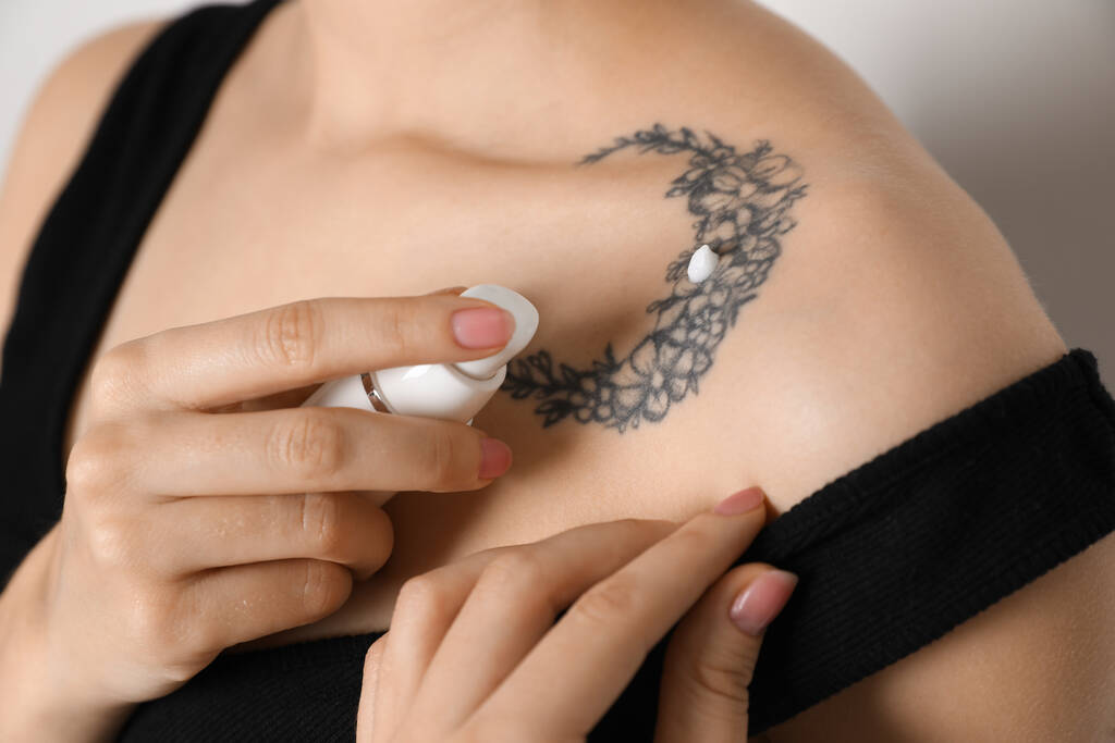 Nainen, joka levittää kermaa tatuointinsa iholle vaaleaa taustaa vasten, lähikuva - Valokuva, kuva