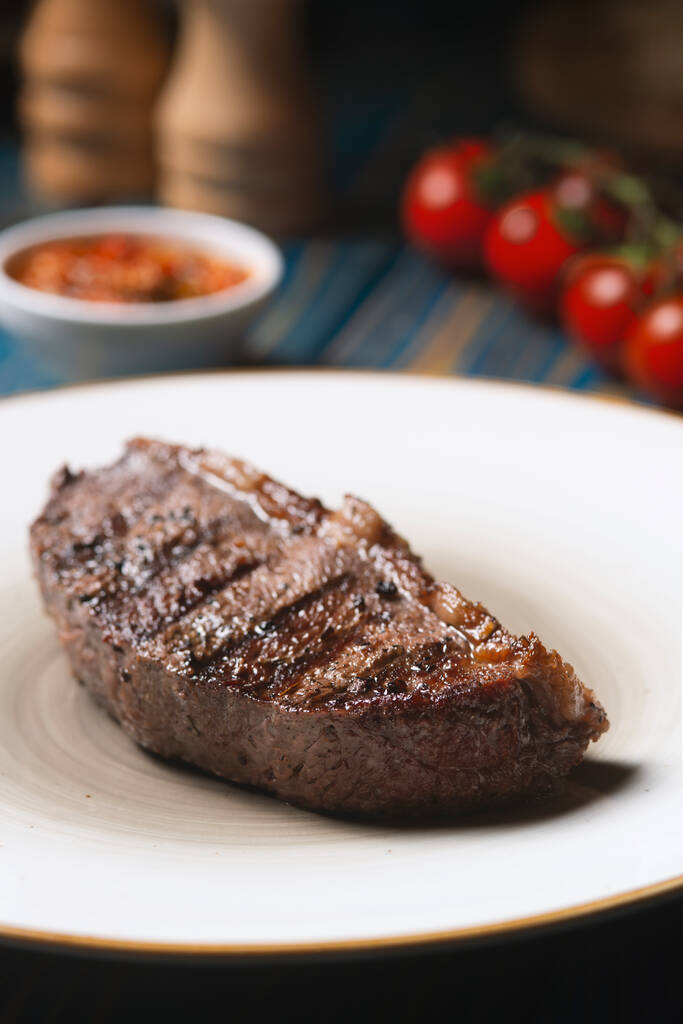 Gebratenes Steak, Kirschtomaten, Salz und Pfeffer auf blauem Holztisch. - Foto, Bild