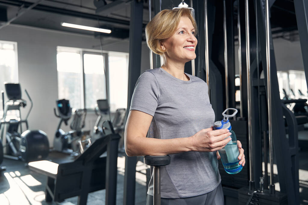 Sportowa kobieta z butelką wody stojąca na siłowni - Zdjęcie, obraz