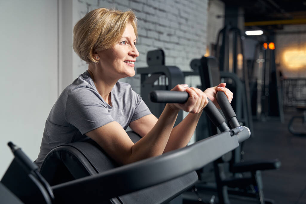 Cheerful woman using gym equipment in fitness center - Photo, Image