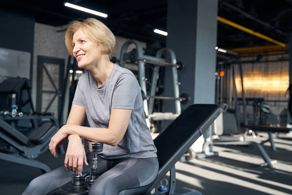 Fröhliche Frau ruht sich nach dem Training im Fitnessstudio aus - Foto, Bild