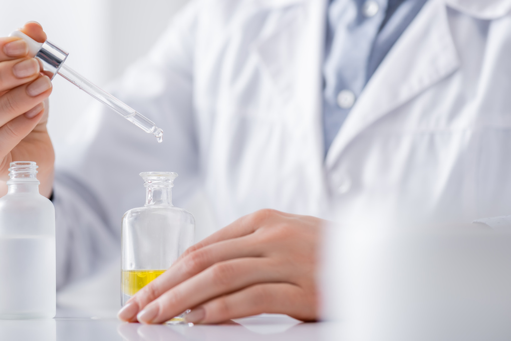przycięty widok asystenta laboratoryjnego trzymającego serum z pipetą  - Zdjęcie, obraz