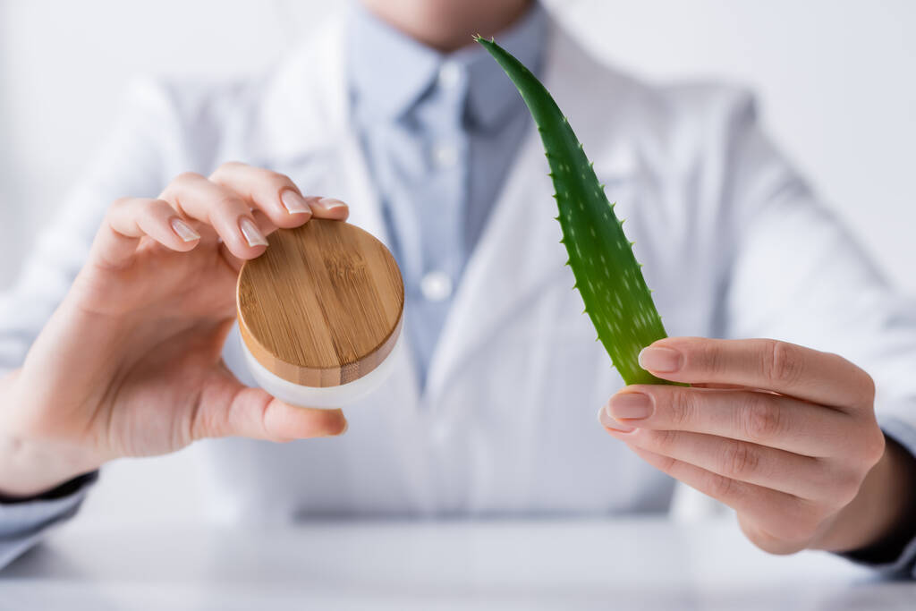 cropped view of laboratory assistant holding aloe and container with cream in lab - Photo, Image