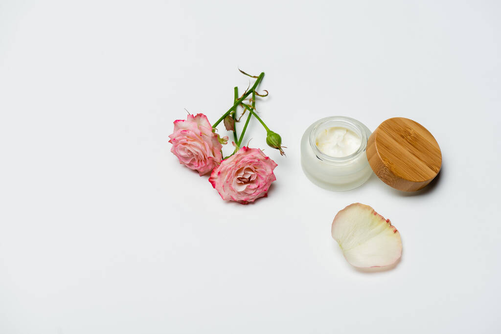 roze bloemen in de buurt van container met crème op wit - Foto, afbeelding