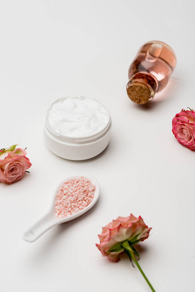 kwiaty w pobliżu różowej soli morskiej, butelka z wodą różaną i pojemnik z kremem na białym - Zdjęcie, obraz