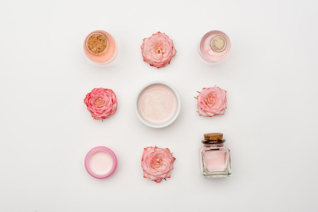 Krema yakınındaki çiçeklerin ve beyaz üzerine kozmetik ürünler konan şişelerin üst görüntüsü - Fotoğraf, Görsel