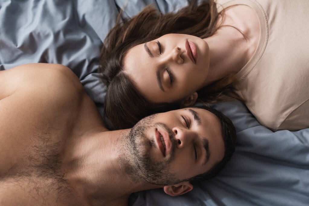Vista dall'alto della donna bruna sdraiata vicino al fidanzato senza maglietta sul letto  - Foto, immagini