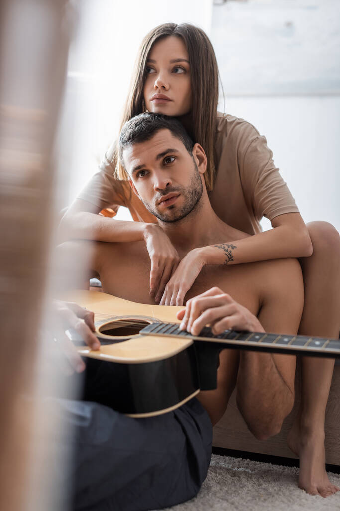 Mujer morena abrazando novio sexy con guitarra acústica en casa  - Foto, imagen