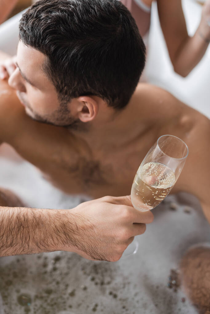 Вид сверху на молодого человека с бокалом шампанского рядом с размытой девушкой в ванной  - Фото, изображение