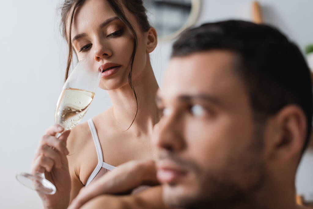 Mujer bonita sosteniendo una copa de champán cerca de novio borroso en casa  - Foto, imagen