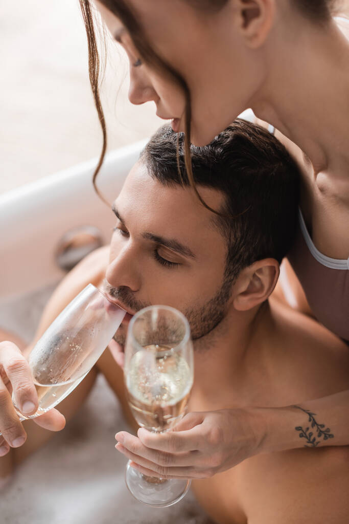 High angle view of muscular man drinking champagne near girlfriend in blurred bathtub  - Photo, Image