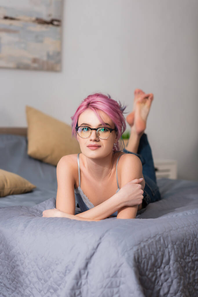 młoda kobieta z różowymi włosami w okularach leżących na łóżku - Zdjęcie, obraz